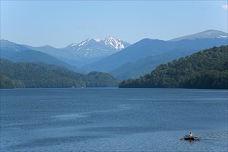 A small boat on a calm blue reservoir with snow-capped mountains in the background, Vidraru