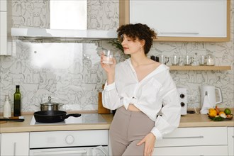 Young woman standing in profile in the kitchen with glass of pure water