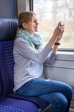 Young woman on a train takes photos of the landscape with her smartphone