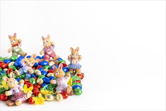 Several Easter bunny figures surrounded by colourful chocolate eggs on artificial grass, white