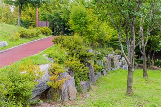 Walking path going uphill behind wall of large boulders in lush urban public park in South Korea