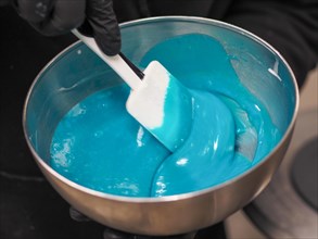 Sweet pastry chef stir a Bright blue icing being stirred with a spatula in a metal mixing bowl for