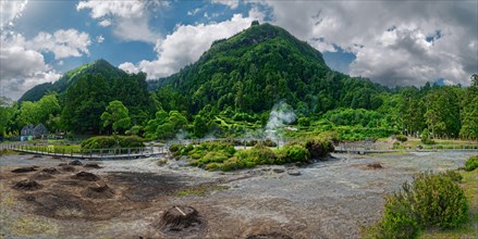 Panoramic view of a geothermal area with steam, surrounded by a forest under a dynamic sky,