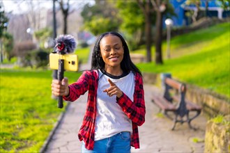 Frontal photo of an african woman vlogging recording a video with mobile from the city