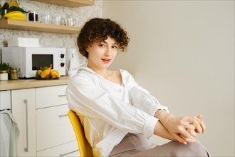 Young woman stretches playfully while sitting on a chair in the kitchen