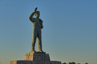 Statue of a man with his arm outstretched towards the sky at dawn, bronze statue of a waving sailor