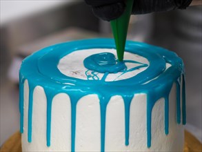 Close-up of a hand wear latex gloves applying blue icing to a white cake using a pastry bag