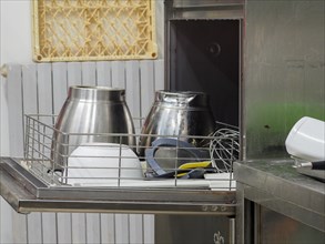An assortment of metal kitchenware lying on a dish washer in an industrial kitchen