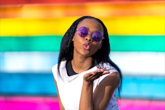 African woman with sunglasses gesturing blowing a kiss in a multicolored vivid urban background