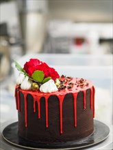 A luxurious chocolate cake with vibrant red icing and roses on a revolving cake stand
