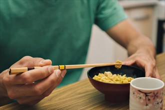 Close-up detail of male hands holding chopsticks eating rice from a bowl. Concept of traditional