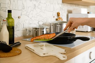 Closeup view of female hand holding fried trout steak on a spatula over the serving board in the