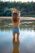 Back view of a woman standing in the river takes off her shirt