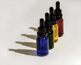 Four glass eye dropper bottles filled with blue, green, yellow and red liquid casting dark shadows