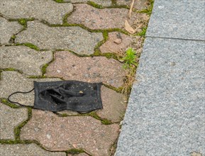Discarded dirtied black medical face mask on brick sidewalk