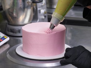 Confectioner with black gloves icing a pink cake with a pastry bag in a precise manner