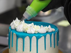 Decorating a cake with white icing using a pastry bag, with blue frosting dripping