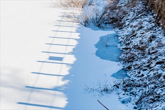 Shadow of wooden fence posts on white surface of frozen lake near shoreline in South Korea
