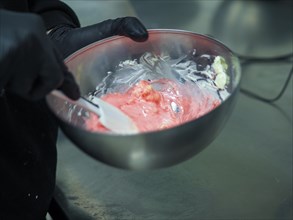 Pastry chef wearing black gloves for hygiene Stirring pink frosting in a steel bowl with a white