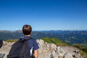 Hiking in the Allgaeu Alps: A young boy looks out over the Alpine foothills from the summit of the