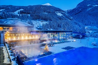 Snow-covered rock spa in winter, thermal bath with Christmas lights at dusk, Bad Gastein, Gastein