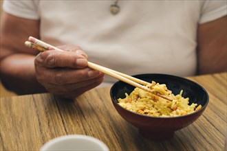 Close-up detail shot of an woman's hands eating rice and vegetables with chopsticks