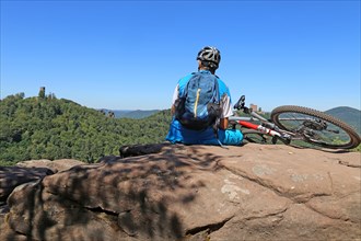 Mountain biker in the Palatinate Forest on a rock with a view of Trifels Castle, Annweiler