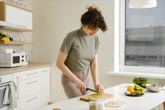 Cheerful young woman makes vegetable salad and cutting celery in the kitchen