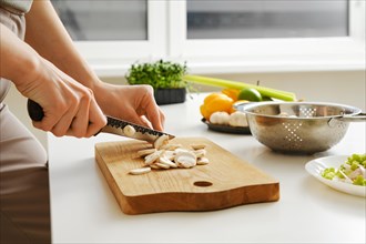 Unrecognizable woman slicing fresh champignon in the kitchen on wooden cutting board