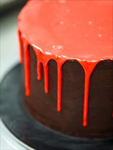 A chocolate cake with red dripping icing on a black surface, creating a sense of celebration