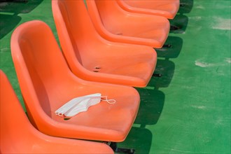 White medical face mask left on empty orange stadium seat at sports center