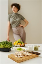 Kitchen table with fresh organic vegetables and blurred young woman on background leaning against