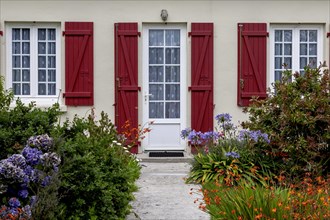 House facade with mullioned windows, entrance door, red shutters and flower beds, Ile de Brehat,