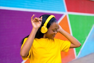 Portrait of a cool african young woman with yellow headphones and t-shirt dancing next to vivid