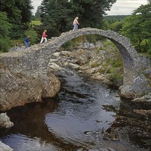 Three women walk across the packhorse bridge at Carrbridge in Scotland, Great Britain, Europe.