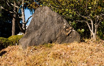 Large triangular boulder on side of hill covered with brown autumn grass