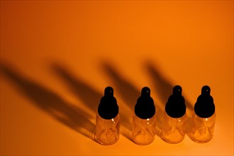 Four glass eye dropper bottles with dark black shadows on golden orange background. A little noise