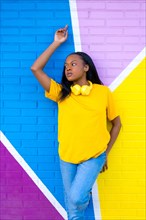 Vertical portrait of an african young woman posing standing and looking aside on a colorful wall