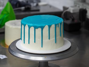 Fully iced white cake with blue drips on a rotating cake stand