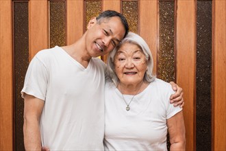 Happy older Asian mother and adult son hugging affectionately, looking at camera, smiling, enjoying