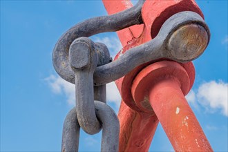 Closeup of linchpin attached to large red anchor with blue cloudy sky in background in Yeosu, South