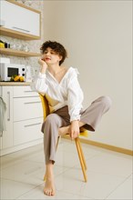 Young woman sits thoughtfully on a yellow chair in a well-lit, contemporary kitchen, embodying a