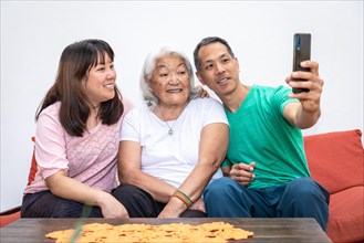 Adult children and elderly white haired mother, ethnic Japanese family, take a selfie sitting on a