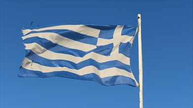 The Greek flag fluttering in the wind on a mast, against a clear blue sky, Gythio, Mani,