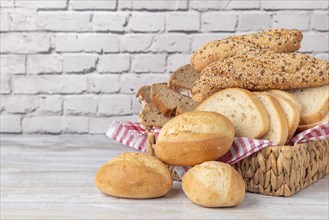 Various types of bread and pastries in a basket on a wooden table in front of a white brick wall,