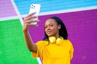 Cute african woman taking a selfie with a mobile phone standing next to multicolored wall