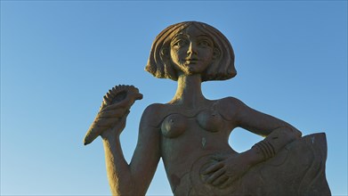 A female statue holding up a palm, mermaid, against a clear blue sky, Gythio, Mani, Peloponnese,