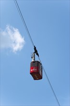 Red cable car gondola hanging on a rope against a clear blue sky with few clouds, Balea Cascada