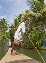 A man navigates a boat through the canals of the Kerala Backwaters using a long pole, Vembanad