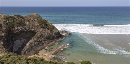 Atlantic Ocean waves breaking on rocky headland and bay with sandy beach, Praia de Odeceixe,